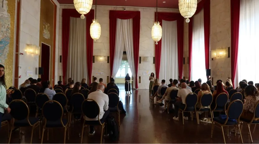 An audience in a grand hall with chandeliers