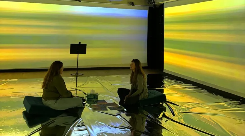 Two participants on cushions inside the Waves of Us installation, in yellow light
