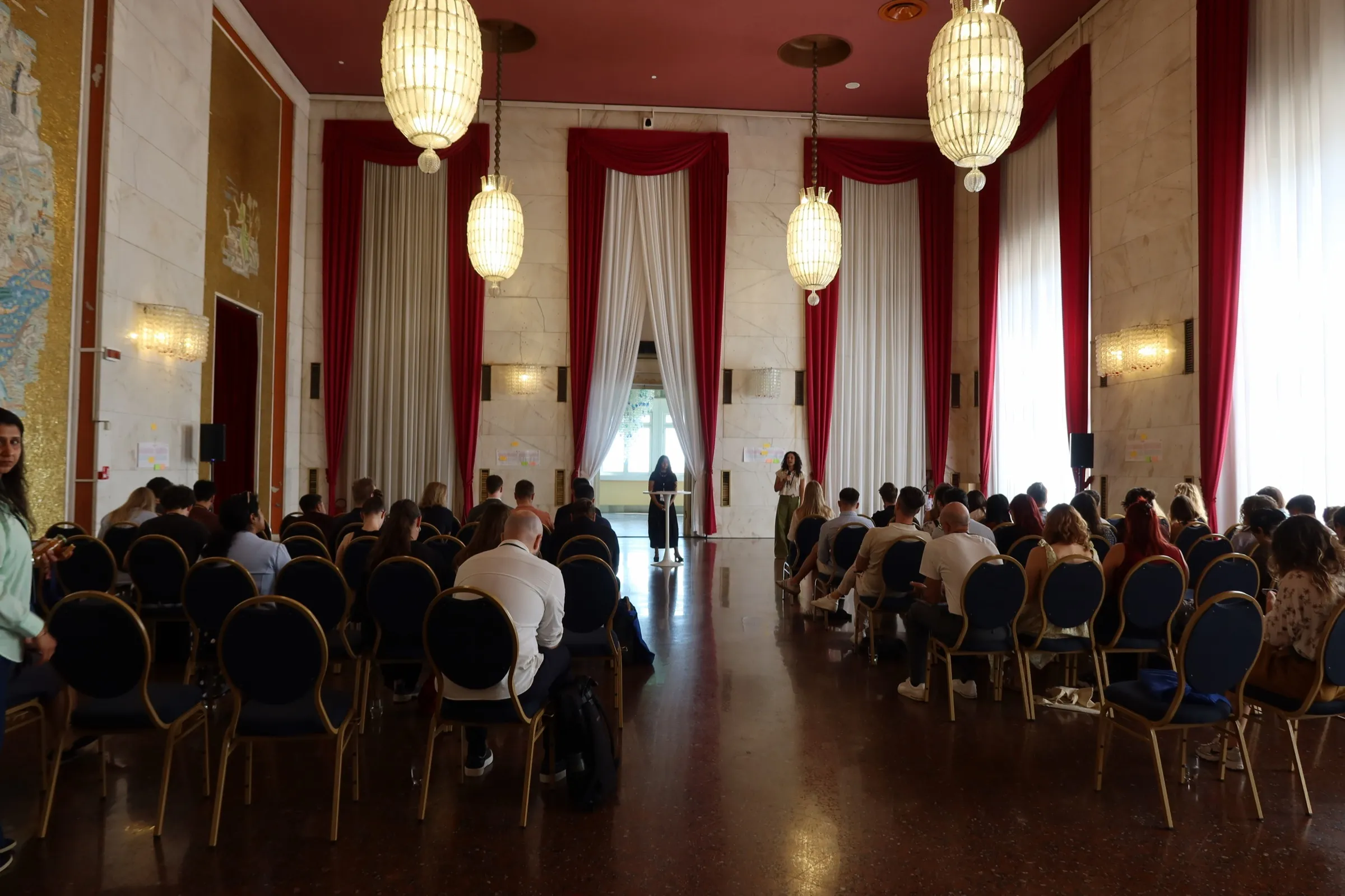 Sana speaking to an audience in a grand hall